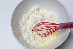 Farmers cheese added into whisked eggs in a large bowl