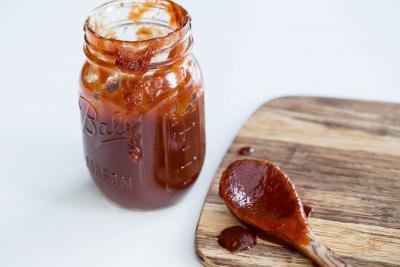 Homemade BBQ Sauce in a jar with a wooden spoon on the cutting board