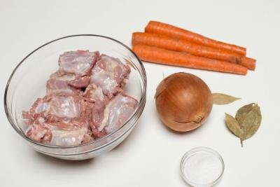 Ingredients on the table including; a bowl of turkey necks, an onion, a little bowl with salt, bay leaves, and 3 carrots