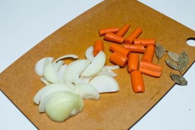 Carrots cut into large pieces, onions cut into half rings and bay leaves all on a cutting board