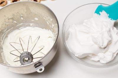 Truwhip being added from a bowl into the mixing bowl with the cream cheese mixture in the KitchenAid mixing bowl