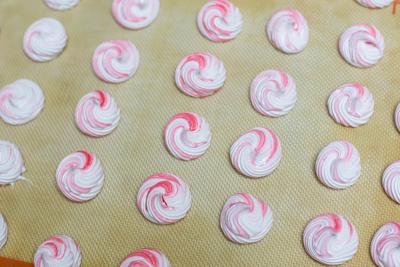 Meringue cookies piped out on the a baking sheet lined with a silicon mat