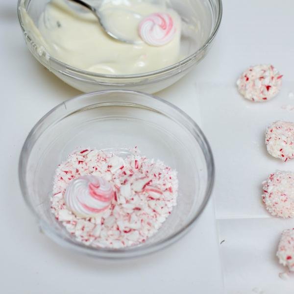 Meringue cookie first being dipped into the bowl of melted white chocolate and then into the pieces of broken candy cane