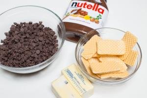 Ingredients on the table including; chocolate chips in a bowl, wafers in a bowl, 2 sticks of butter and jar of nutellla