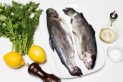 Ingredients on the table including; 2 lemons, parsley and dill, 2 trouts, oil, salt and pepper