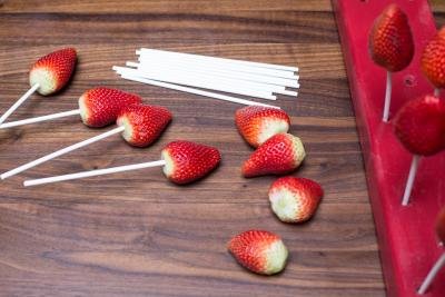 Lollipop sticks being placed into the top of the strawberries