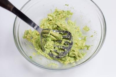 Avocado in a bowl being mashed with a potato masher