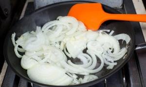 half ring onions being caramelized on a skillet