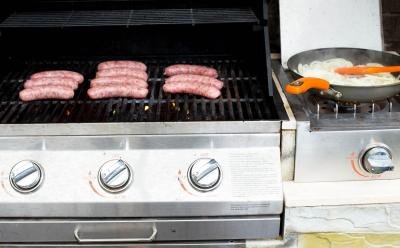 Johnsonville Beer Bratwurst being grilled on a grill with a skillet with onions besides it