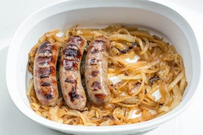 A ceramic baking pan filled with caramelized onions and Johnsonville Beer Bratwurst sausages placed on top