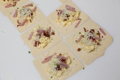 Ham, cheese, scrambled eggs, green onion and bacon placed into the center of every puff pastry square