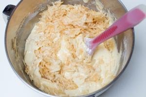 Grated apples being added into cake batter in a mixing bowl