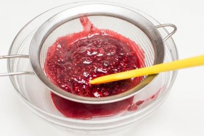Raspberry mixture being strained through a strainer into a bowl