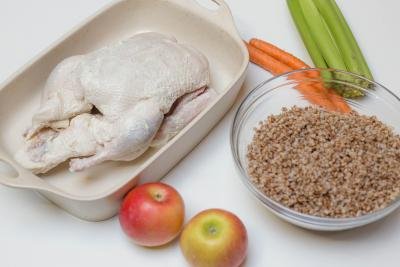 Seasoned duck in a ceramic baking pan, 2 apples, 2 carrots, celery, and buckwheat in a bowl