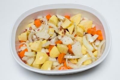 Seasoned veggies and bacon spread on the bottom of a ceramic baking dish