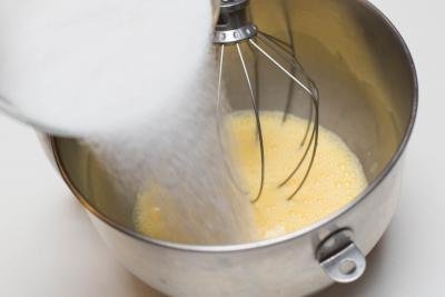 Sugar being poured into the KitchenAid mixer with the eggs
