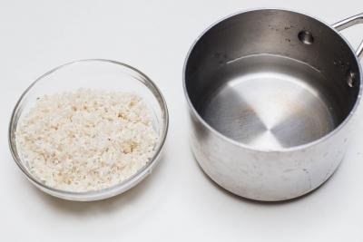A bowl of rice in a bowl and a pot of water besides the bowl