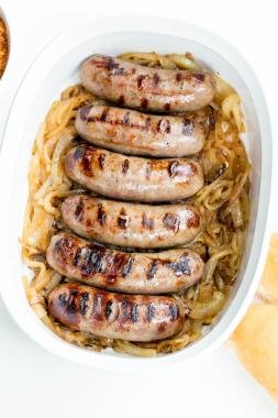 Johnsonville Beer Bratwurst on top of caramelized onions in a ceramic baking pan