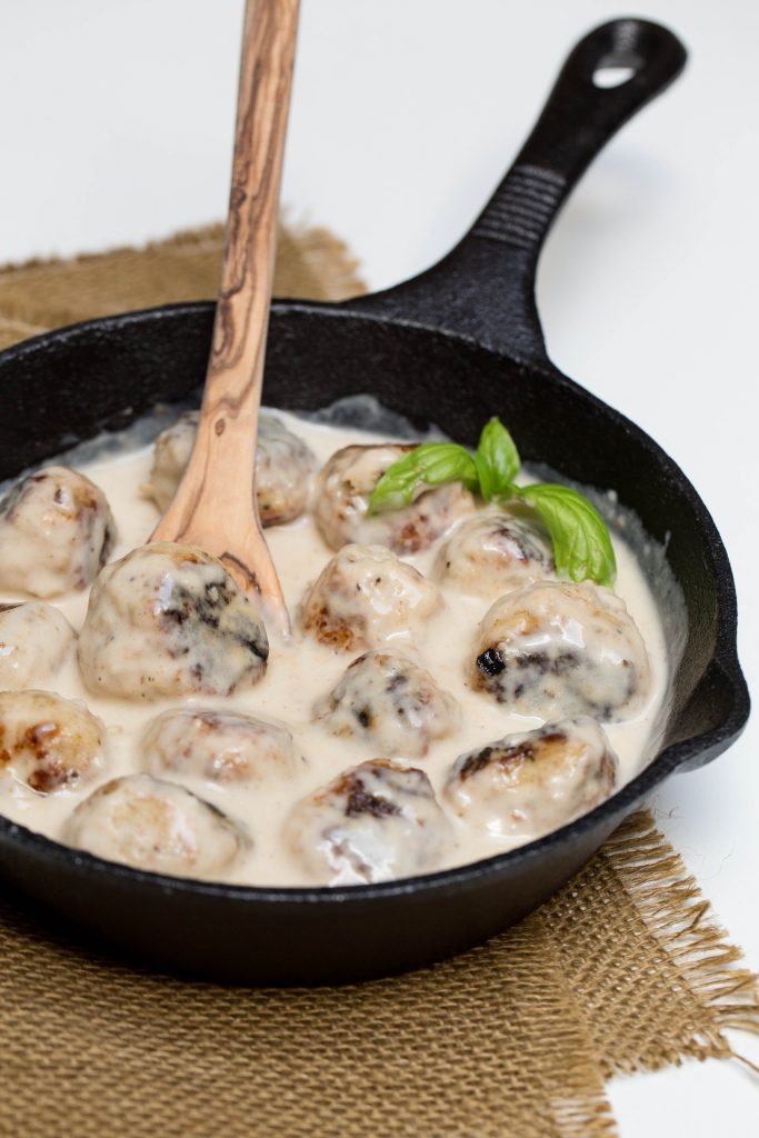 Meatballs in a Cream Sauce in a small iron cast pan with a wooden spoon in the sauce
