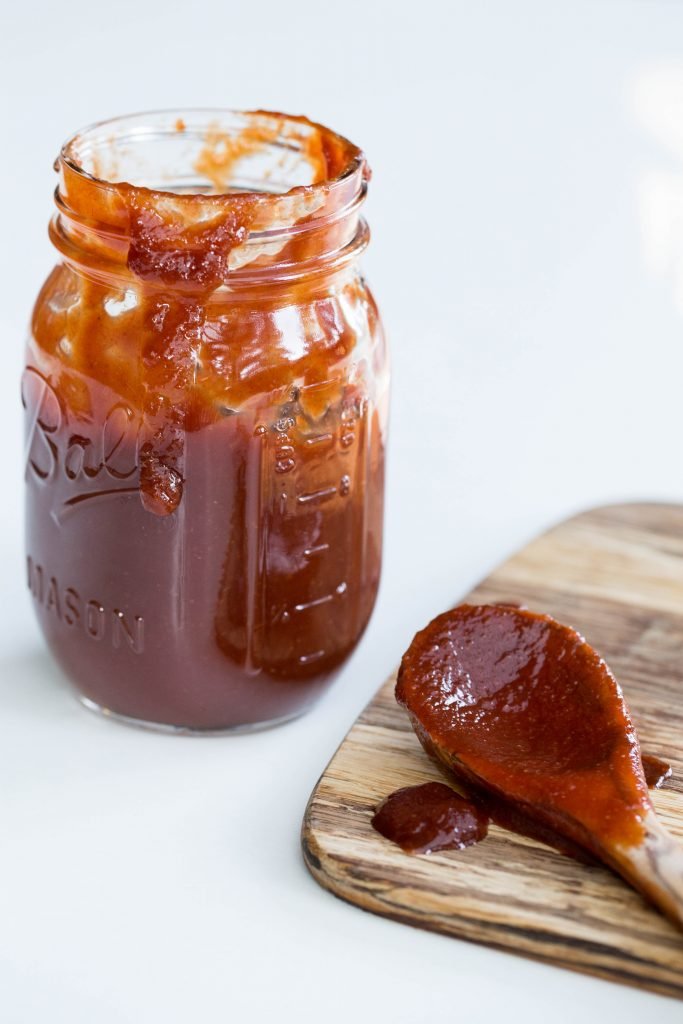 Homemade BBQ Sauce in a jar with a wooden spoon on the cutting board