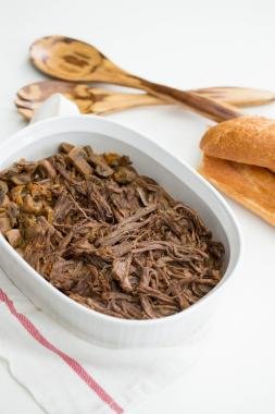 Slow Cooker Beef Roast in a baking pan with bread and 2 wooden spoons next to it