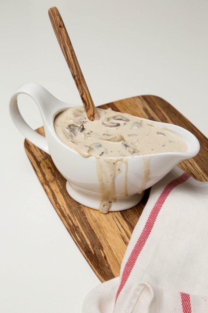 Creamy White Wine Mushrooms in gravy boat on cutting board with a spoon inside