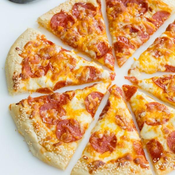 Pepperoni pizza on a cutting board cut into slices with a pizza slicer besides it