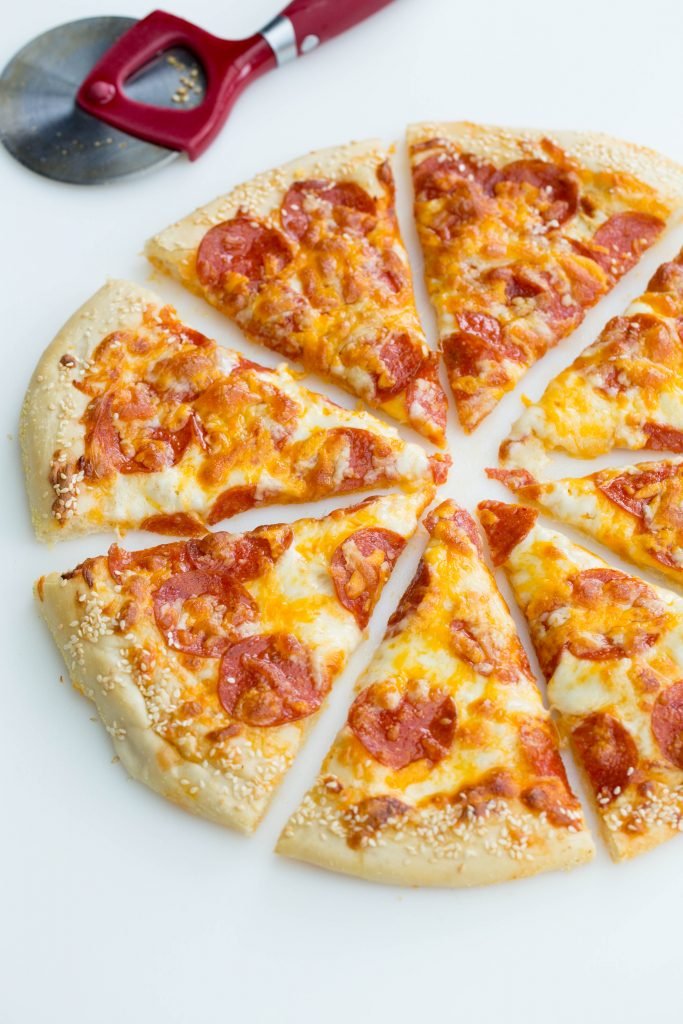 Pepperoni pizza on a cutting board cut into slices with a pizza slicer besides it