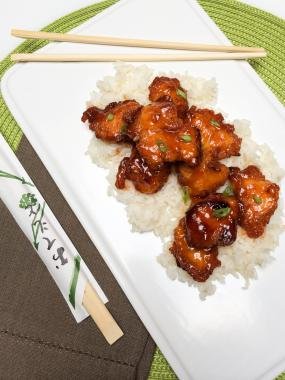Sweet and Sour Chicken on rice on a plate with chopsticks besides the plate