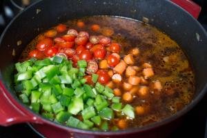Green peppers, tomatoes and carrots added into a pot with beef, onions and water