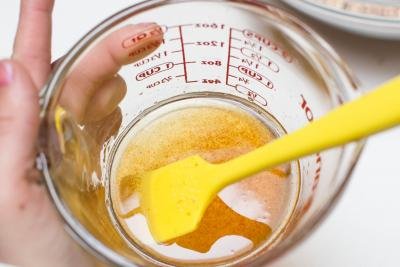 Vanilla extract, honey, and coconut oil combined in a measuring cup with a spatula