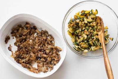 A ceramic baking pan with sautéed mushrooms and onions and a bowl with sautéed zucchini