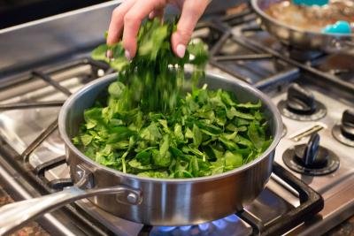 Spinach being added into the pot with sautéing veggies
