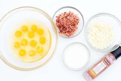 4 bowls each with the following ingredients; eggs, bacon, mozzarella cheese, and whipping cream also a package of Himalayan pink salt