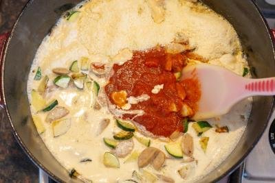 Whipping cream, tomato sauce added into the iron cast pot with zucchini and sausage
