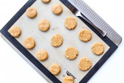 Cookies on a baking pan with fork besides them to make a design on top of the cooke