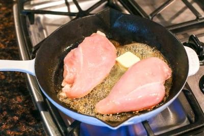 Chicken cooking in a skillet with butter.