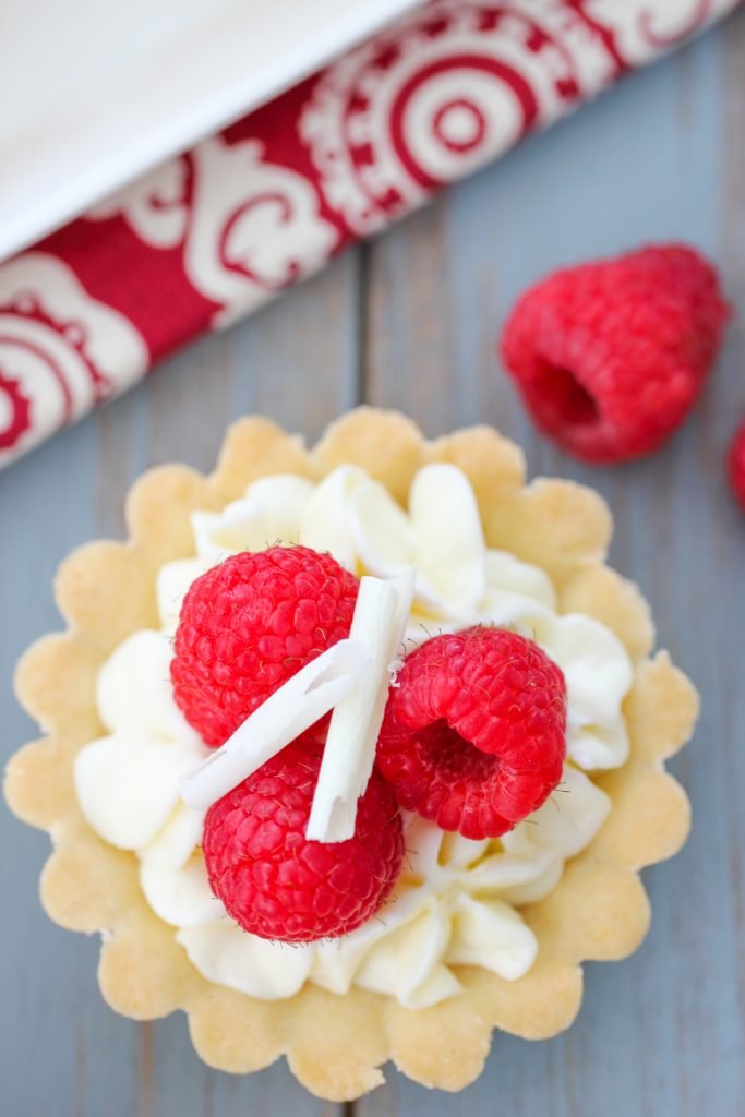 Tart on a wood board with bowl and raspberry in background.