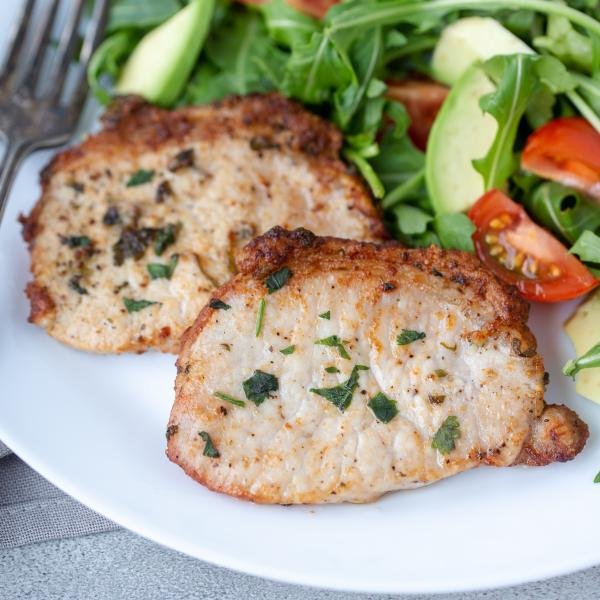 air fryer pork chops on a plate with a fork and a salad besides the pork