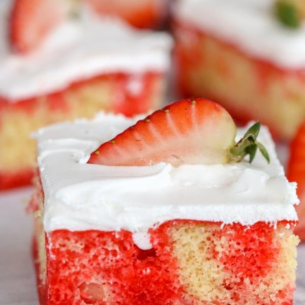 Strawberry Jello Poke Cake square piece with more pieces behind it in the background
