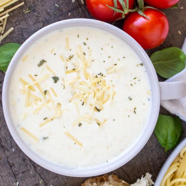 Homemade Alfredo Sauce in a bowl with parmesan with bread and pasta in the background