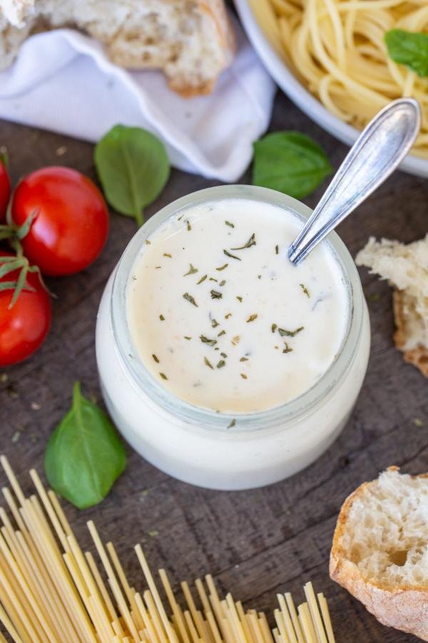 Homemade Alfredo Sauce in a jar with parmesan with bread and pasta in the background