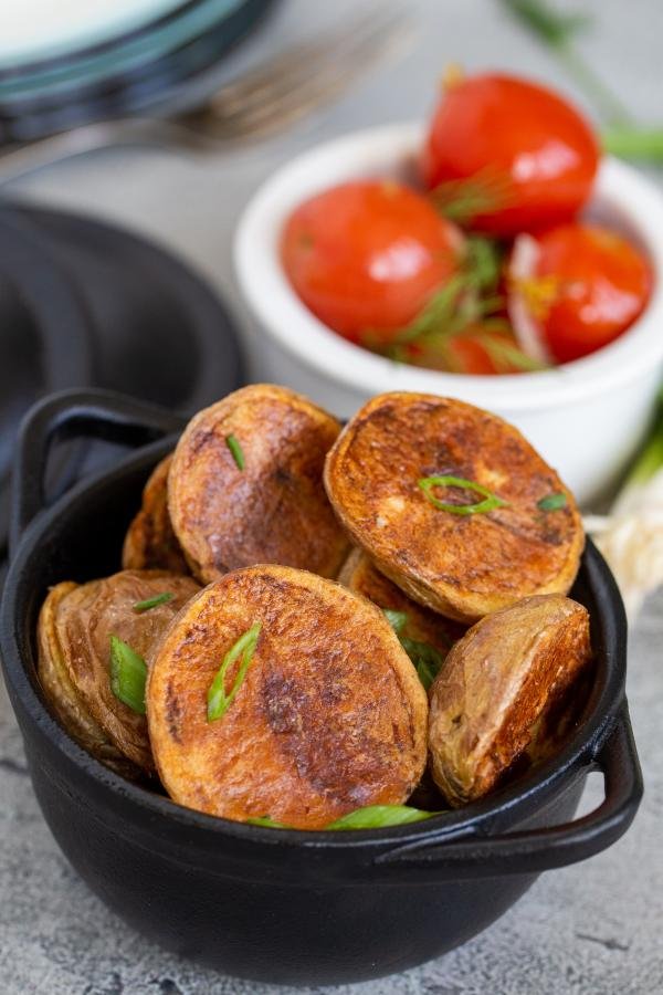 Potatoes in a pot with a bowl of tomatoes in background 