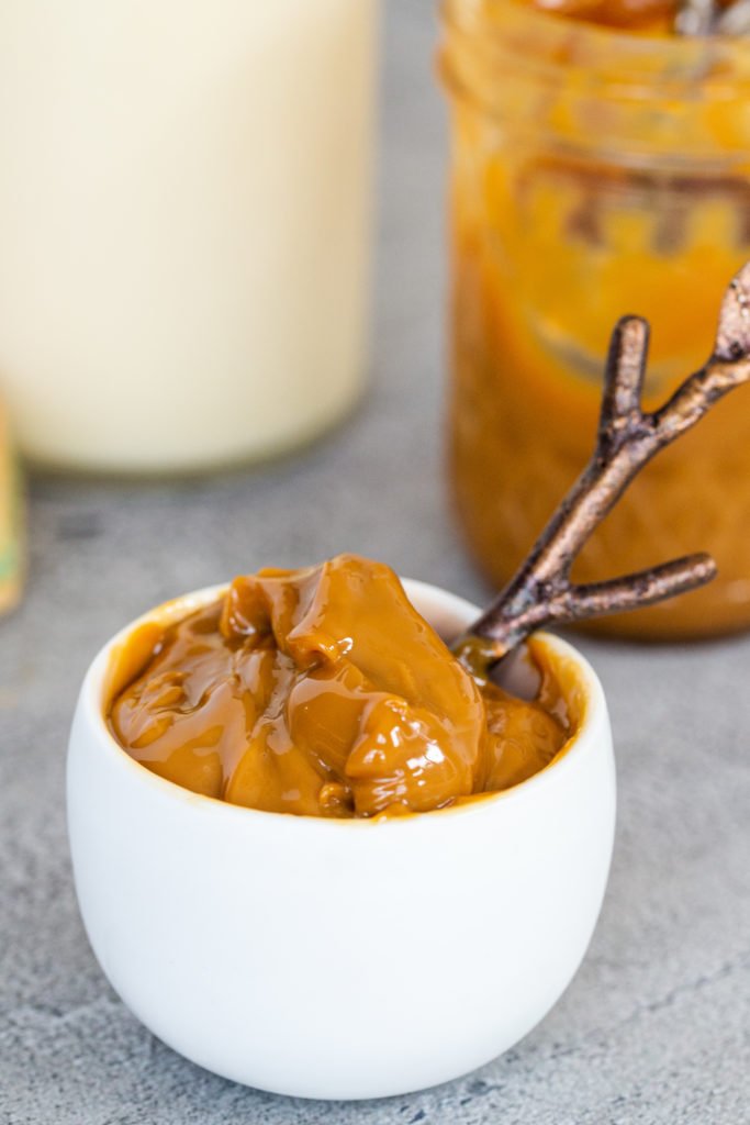 Bowl with spoon and dulce de leche in it, jar in the background