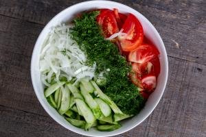 Sliced cucumbers, tomatoes, onion and dill in a bowl.