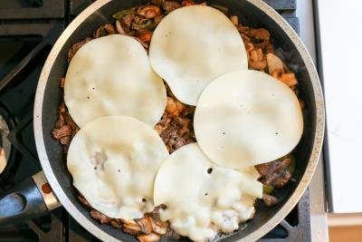 Skillet with melted cheese over vegetables and steak