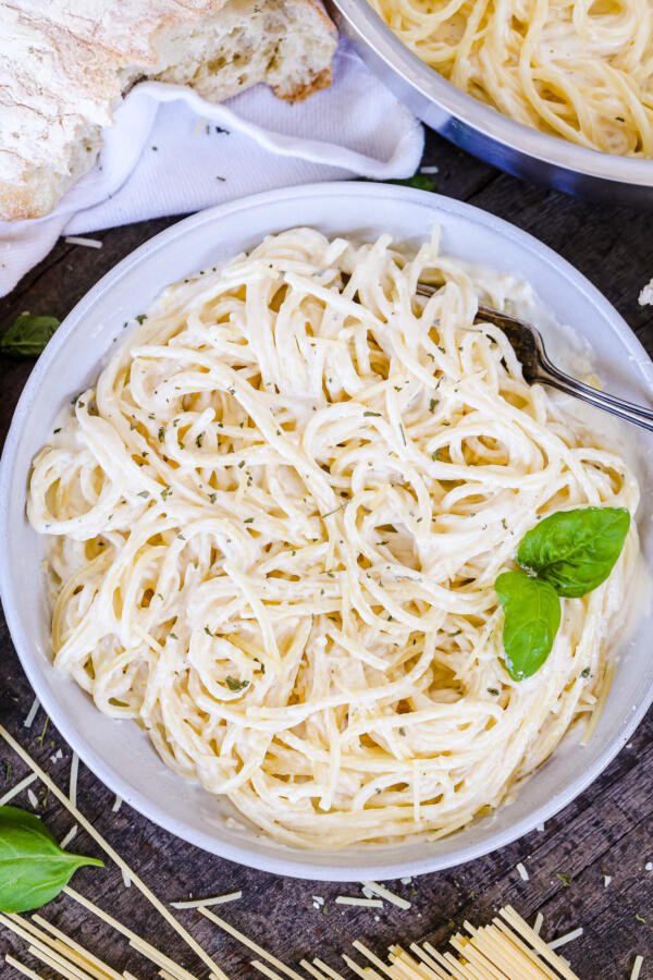 Alfredo pasta in a plate with bread, cheese and pasta next to it. 