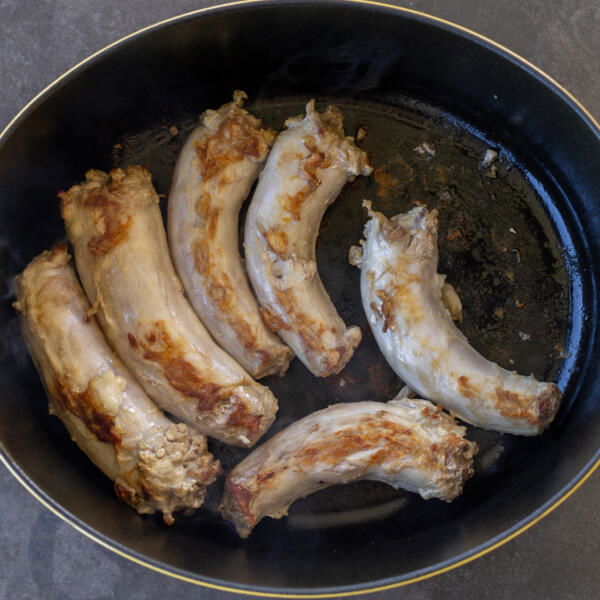 Turkey necks frying in a pan.