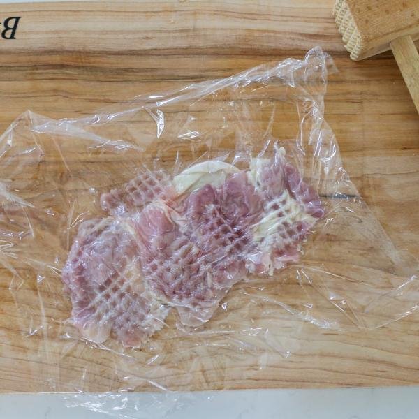 chicken getting tenderized on a cutting board