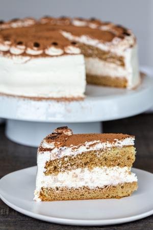 A slice of Tiramisu on a plate with a cake behind it